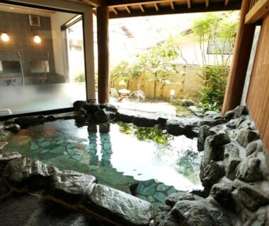 Indoor rock-lined onsen bath with wooden interior and garden view at Irorino Yado Sankichi Shizuoka