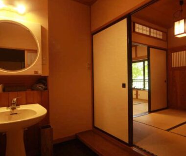 Wash basin and mirror leading to tatami room with shoji doors and greenery visible beyond