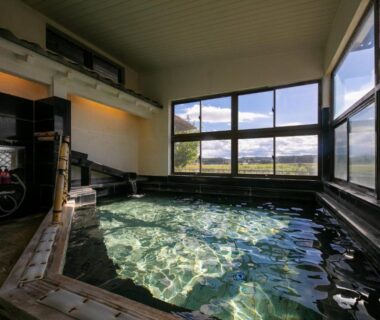 Wood-framed indoor onsen with large windows overlooking fields and distant mountains in Tochigi