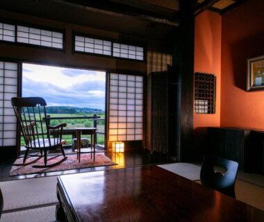 Tatami room with low table, shoji screens and rocking chair on veranda overlooking green fields in Tochigi
