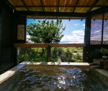 Wooden soaking tub overlooking trees and blue sky at Isamikan ryokan, Tochigi, Kantō, Japan
