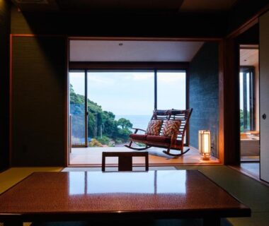 Tatami-floored room with low table, sliding doors and balcony chairs overlooking greenery and distant horizon