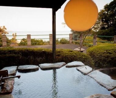 Stone onsen bath under roof with lantern, garden and sea view at Isaribi ryokan, Shizuoka, Chūbu, Japan