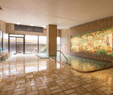 Spacious tiled indoor onsen with decorative mural and low soaking pool at Isawa Tokiwa Hotel, Yamanashi