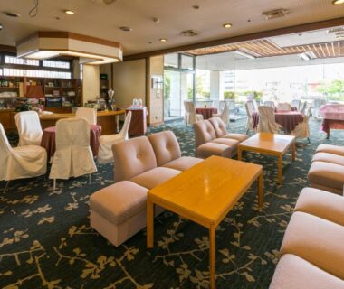 Spacious lounge with sofas, low wooden tables, patterned carpet and large windows overlooking courtyard garden