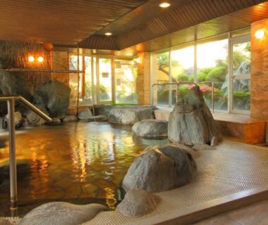 Spacious indoor onsen with rock features and large windows at Isawa View Hotel in Yamanashi