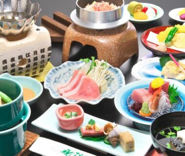 Assorted traditional Japanese dishes with sashimi, small bowls, rice pot and simmered vegetables on lacquered table setting