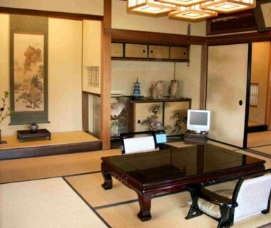 Traditional tatami room with low lacquered table, zabuton chairs, tokonoma alcove and small television at Ise Todaya Ryoan Mie
