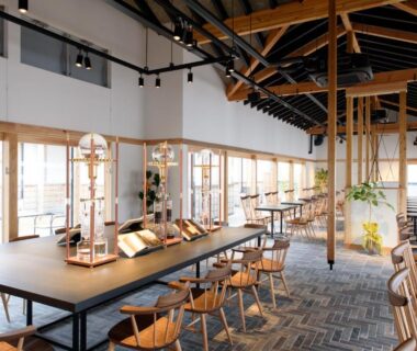Bright communal dining lounge with long wooden table, exposed beams, chairs and large windows at Isegekusando Iseshinsen, Mie