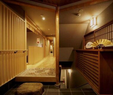 Warm-lit ryokan entrance corridor with wooden paneling and shoji screens at Ishibekoji Muan, Kyoto