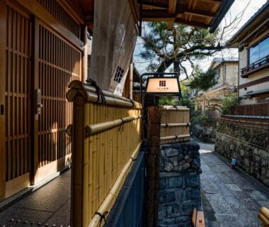 Narrow stone walkway and bamboo fence leading to Ishibekoji Muan entrance in a Kyoto lane