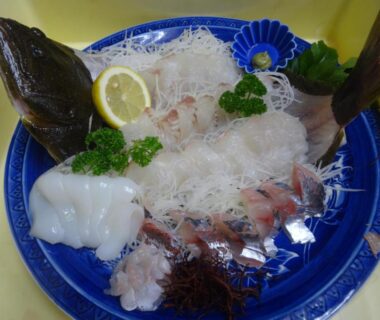 Assorted sashimi on blue plate with shredded daikon, lemon garnish, sliced white fish and squid