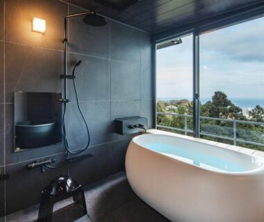 Modern bathroom with freestanding tub and shower, large window framing coastal view and treeline at Ishinoya Atami, Shizuoka