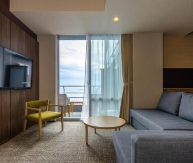 Modern guest room with sofa and balcony overlooking the sea at Ishinoya Atami, Shizuoka