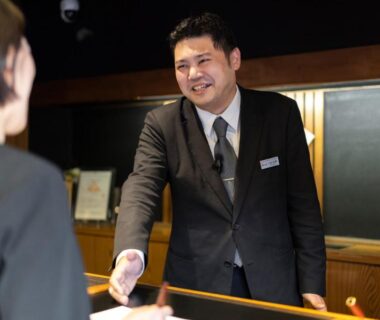 Ryokan receptionist smiling and shaking hands with guest at front desk in Ishinoya Izunagaoka, Shizuoka