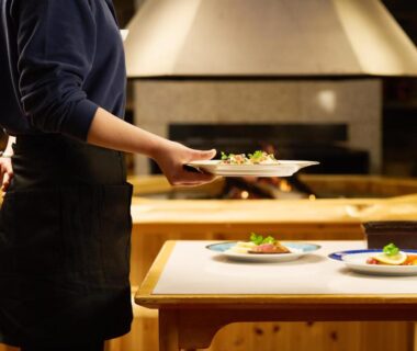 Server placing plated dishes on wooden dining counter at Ishinoyu Lodge in Nagano