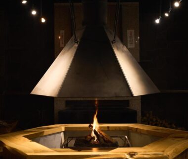 Central wooden irori hearth with suspended metal hood and glowing fire at Ishinoyu Lodge in Nagano