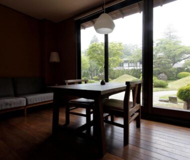 Wooden-floor sitting area with low table and large windows overlooking manicured garden at Itamuro Onsen Daikokuya, Tochigi