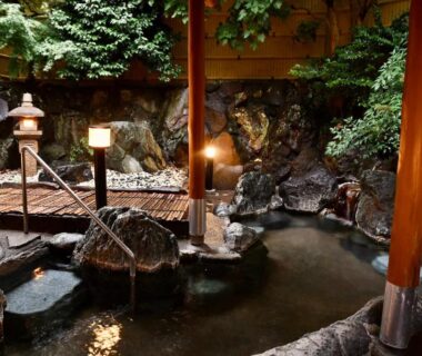Rock-lined onsen bath with wooden posts, stone lantern and small bridge at Ito Kowakien in Shizuoka