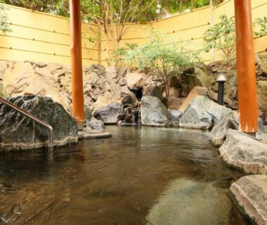 Rock-lined outdoor onsen bath with wooden posts and garden at Ito Kowakien, Shizuoka