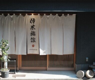 Traditional noren and wooden sliding doors at Ito Ryokan entrance with potted plants and stone lantern, Tokyo