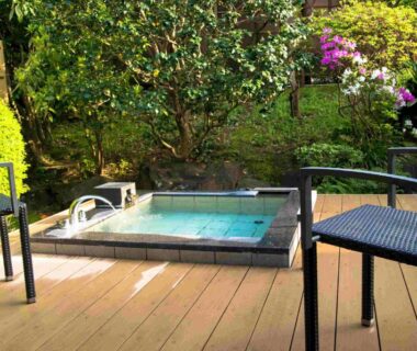 Wooden deck with small tiled outdoor bath, two chairs and surrounding garden at Ito Ryokuyu in Shizuoka