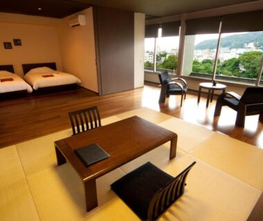 Spacious tatami room with low table, floor chairs, futon bedding and large windows overlooking green hillside