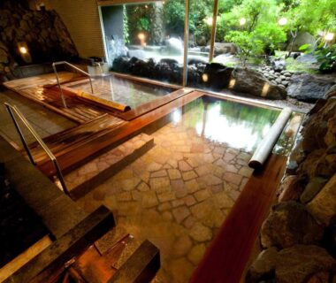 Wooden indoor onsen baths with stone floor and garden view through large window at Ito Yukitei in Shizuoka