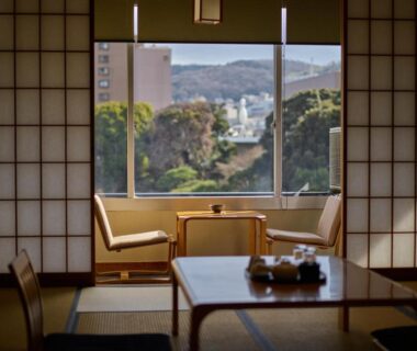 Tatami room with low table and shoji screens, window view of trees and hills at Ito Yukitei, Shūbu, Japan