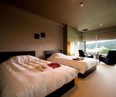 Twin beds and lounge chairs by large window with green hillside view at Ito Yukitei, Shizuoka, Chūbu, Japan