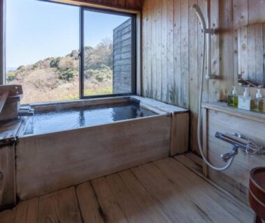Indoor wooden soaking tub with shower fixtures and garden view at Ito Yukitei Kawana Bettei in Shizuoka