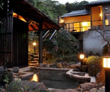 Stone outdoor onsen with lanterns beside a traditional wooden ryokan building in Shizuoka