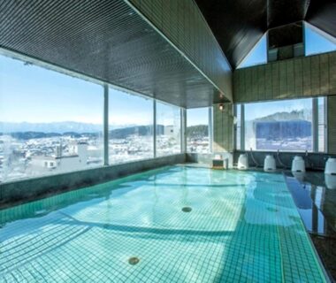 Tiled indoor onsen pool with large windows overlooking Nagano city and surrounding mountains