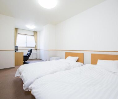 Bright twin room with white bedding, desk and window at Itoen Hotel Asamanoyu in Nagano, Chūbu, Japan