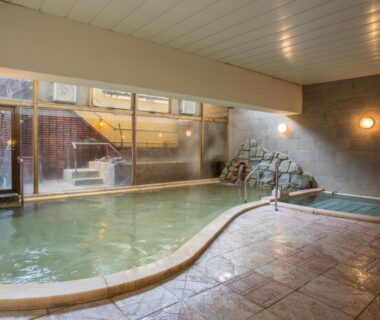 Indoor bathing area with stone feature and large windows at Itoen Hotel Hakone Yumoto, Kanagawa