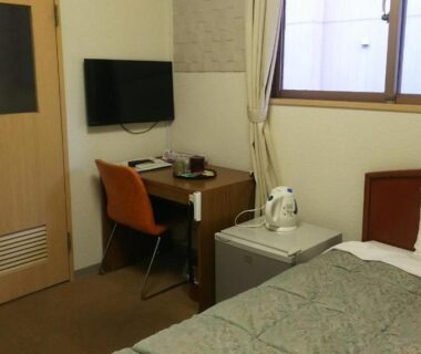 Small single bedroom with bed, desk, wall TV and kettle by window at Itoen Hotel Hakone Yumoto, Kanagawa Japan