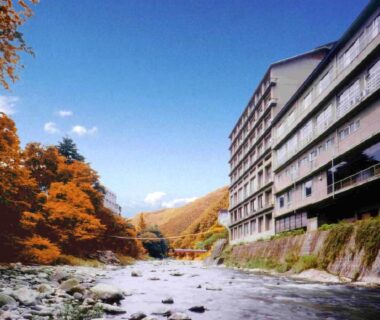 River beside multi-story ryokan with autumn foliage, Itoen Hotel Iizakakanouya, Fukushima