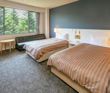 Bright twin guest room with two beds, sofa and large window overlooking trees at Itoen Hotel Kusatsu, Gunma