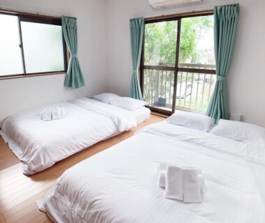 Three low futon beds with white linens and green curtains at Itsukaichi First Villa Hiroshima Chūgoku