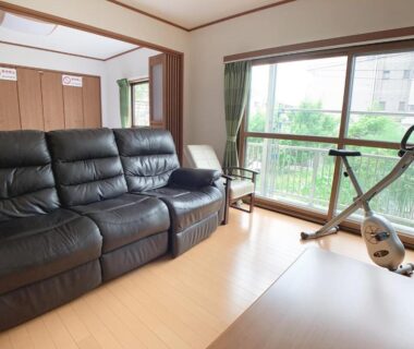 Bright room with black leather sofa, exercise bike, low table and large window overlooking greenery at Itsukaichi First Villa Hiroshima
