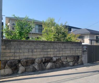 Gated stone wall entrance with residential building visible behind at Itsukaichi First Villa Hiroshima