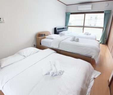 Three single beds with white linens in bright wooden-floored room at Itsukaichi First Villa Hiroshima