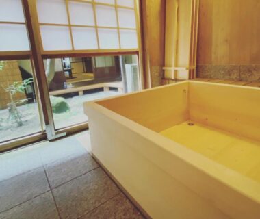 Indoor wooden soaking tub with shoji screens and small courtyard garden at Itsumoya, Hiroshima