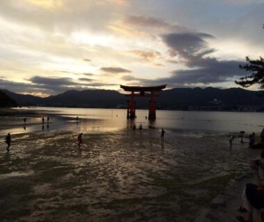 Red torii in shallow tidal flats at sunset, visitors on sand, near Itsumoya, Hiroshima, Chūgoku, Japan