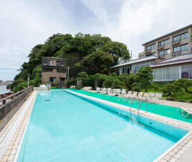 Long outdoor swimming pool beside Iwamotoro with loungers and hillside greenery by the water