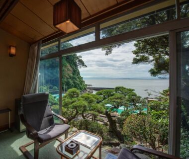Seaside room seating area with low table, manicured garden and sea beyond at Iwamotoro, Kanagawa, Japan