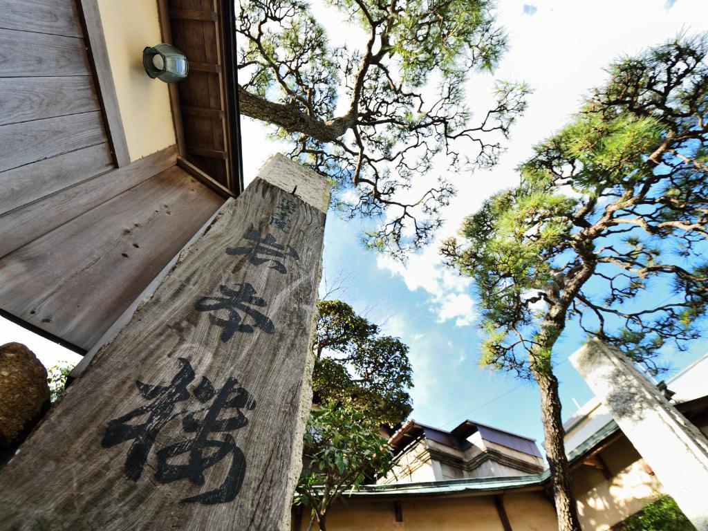 Wooden entrance pillar at Iwamotoro Kanagawa Wooden post inscribed with kanji at ryokan entrance, framed by pine trees and blue sky