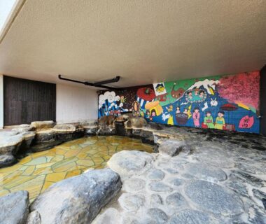 Rock-lined indoor onsen bath with colorful mural at Iwanai Kogen Hotel Hokkaidō