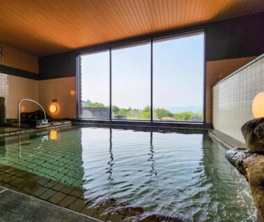 Indoor onsen bath with stone edge and large windows at Iwanai Kogen Hotel, Hokkaidō