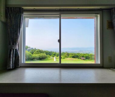 Room window framing grassy hill and distant horizon at Iwanai Kogen Hotel Hokkaidō